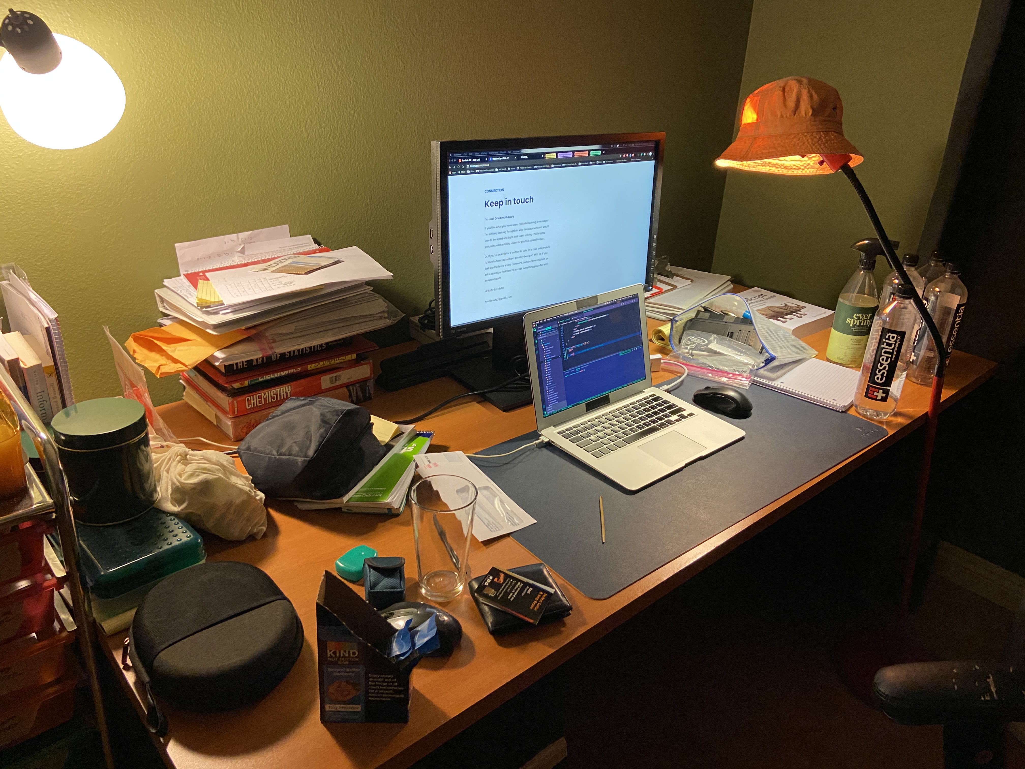 A desk setup with a laptop, monitor, books, and lamps from the year I learned to program.