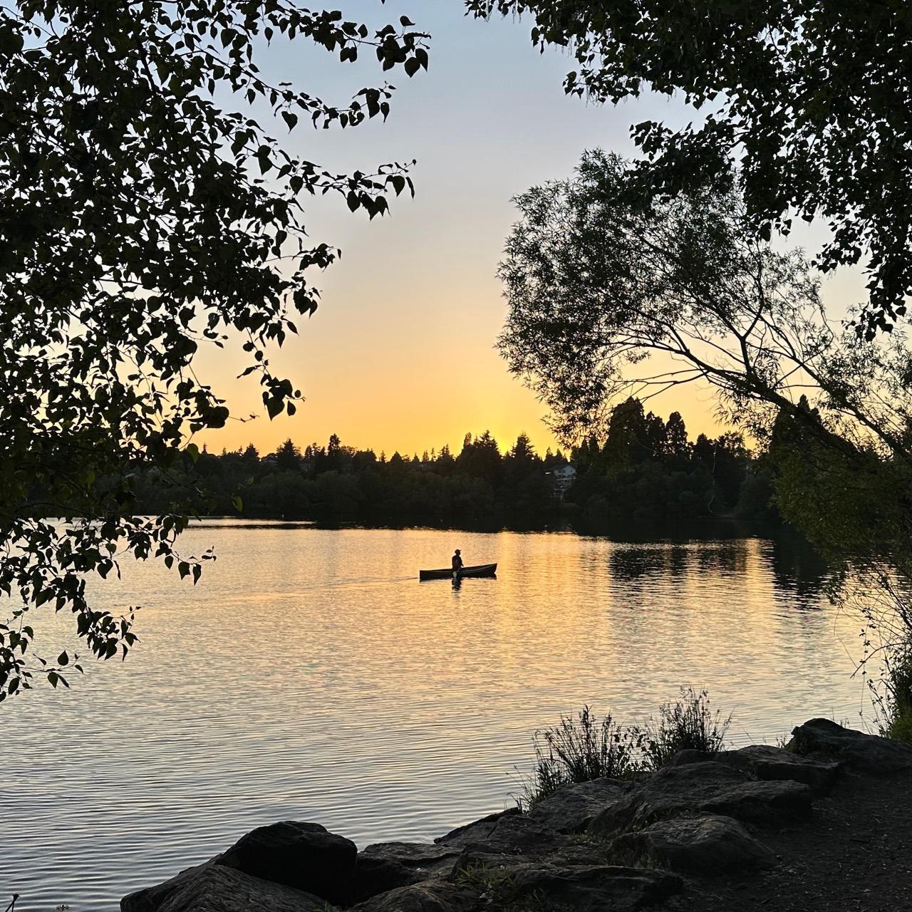 A canoe on a lake at sunset framed by trees.